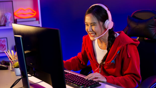 Host channel of beautiful Asian girl streamer concentrating online game wearing headphones pastel color talking with viewers media online. Esport skilled team players in neon blue room. Stratagem.